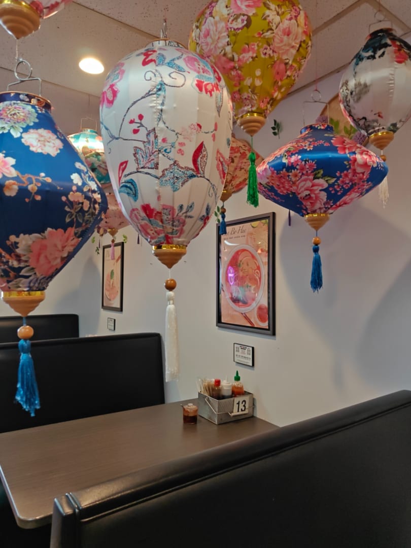 Restaurant interior with black booths, wooden tables, and colorful floral lanterns hanging from the ceiling.