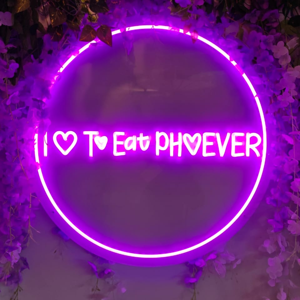 Purple neon sign in a floral setting, reading "I ♡ To Eat PH♡EVER".