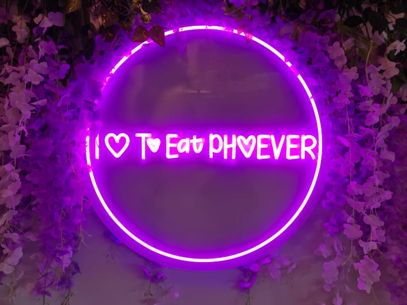 Purple neon sign in a floral setting, reading "I ♡ To Eat PH♡EVER".