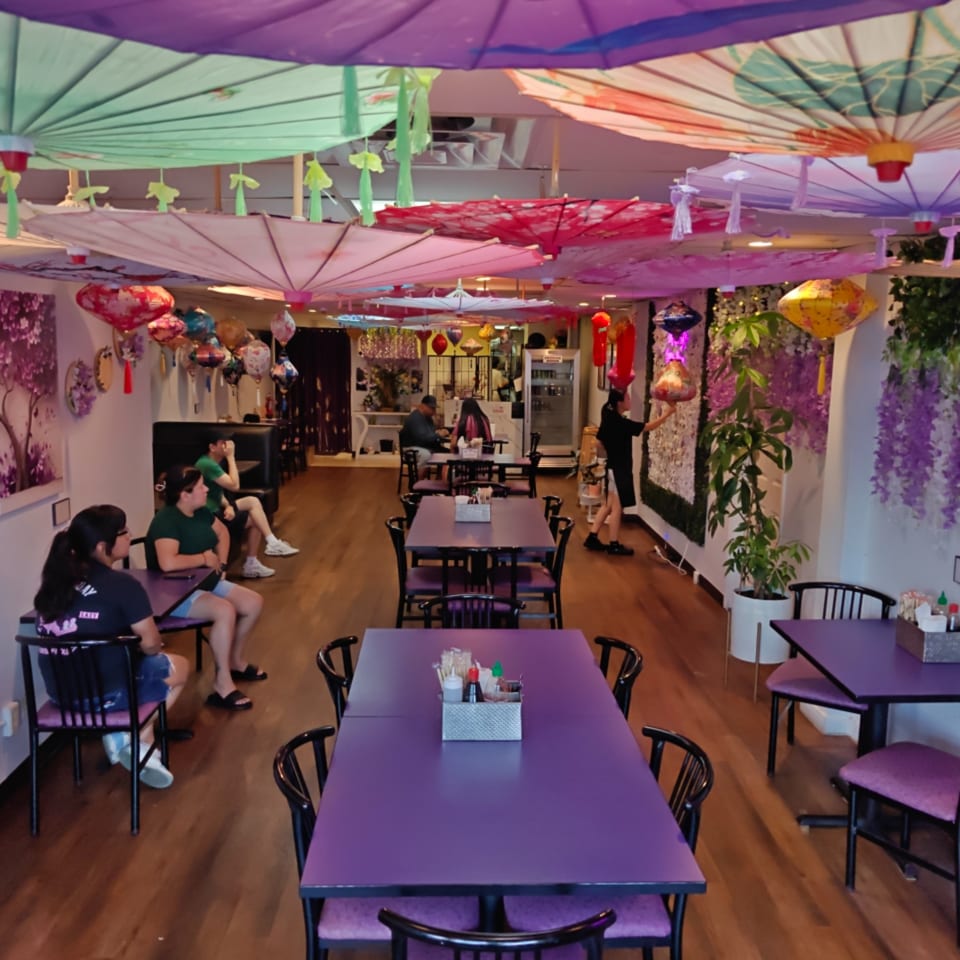 Restaurant interior with purple tables, colorful umbrellas on the ceiling, and customers dining.